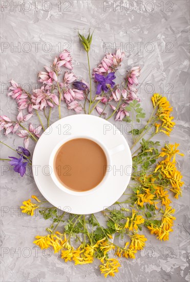 Yellow, pink and blue flowers in a spiral and a cup of coffee on a gray concrete background. Morninig, spring, fashion composition. Flat lay, top view, close up