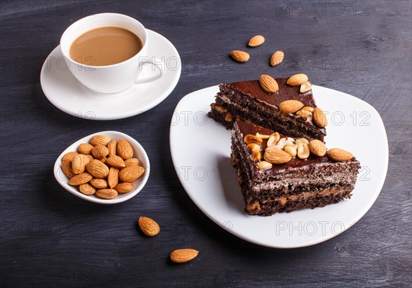 Chocolate cake with caramel, peanuts and almonds on a black wooden background. cup of coffee, close up