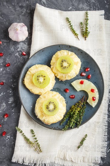 Pieces of baked pork with pineapple, cheese and kiwi on black background, top view