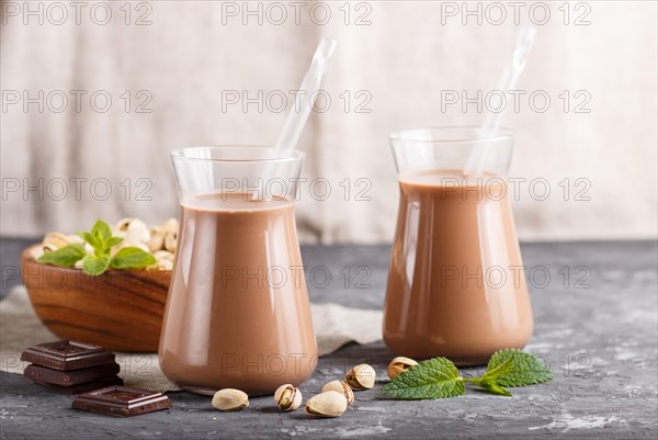 Organic non dairy pistache chocolate milk in glass and wooden plate with pistache nuts on a gray concrete background. Vegan healthy food concept, close up, side view, copy space