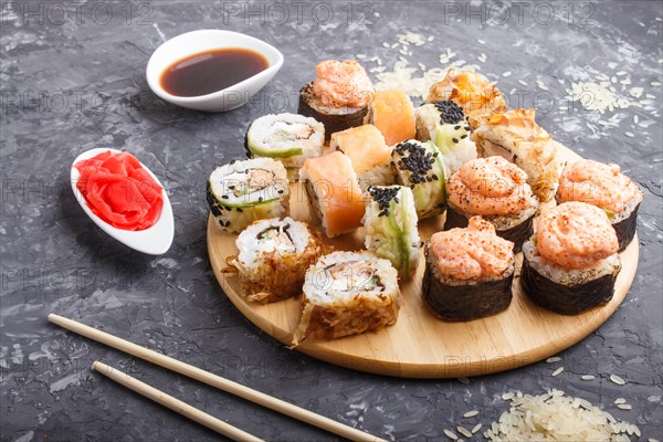 Mixed japanese maki sushi rolls set with chopsticks, ginger, soy sauce, rice on black concrete background. side view, close up, flat lay