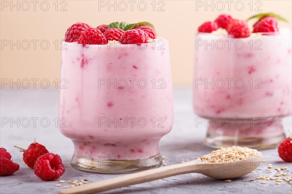 Yoghurt with raspberry and sesame in a glass and wooden spoon on gray and orange background. side view, close up