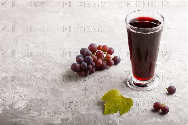 Glass of red grape juice on a gray concrete background. Morninig, spring, healthy drink concept. Side view, copy space
