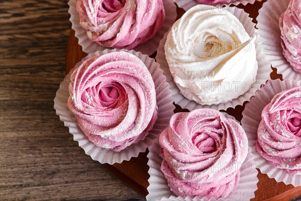 Pink and white homemade marshmallows (zephyr) on a round wooden board on a gray wooden background. top view