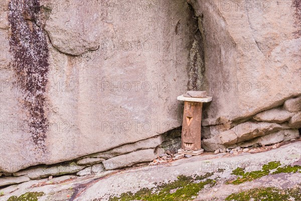 Log held in place with stones and carved to have one eye and mouth on rocky ledge of cliff face in countryside in South Korea