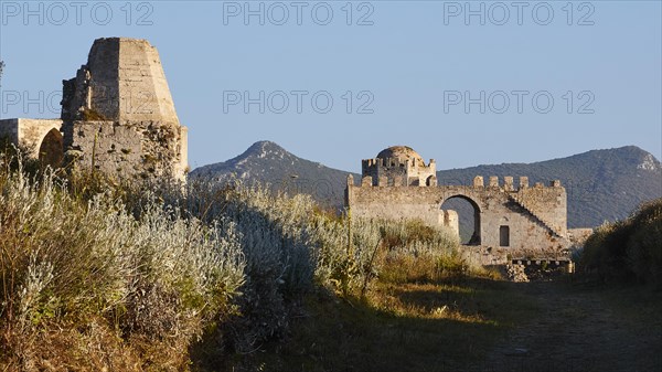 Fortress ruins with overgrown plants and mountains in the background under a blue sky, sea fortress Methoni, Peloponnese, Greece, Europe