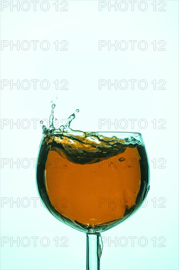 Energetic splashes in a wine glass with orange-coloured liquid create a dynamic scene