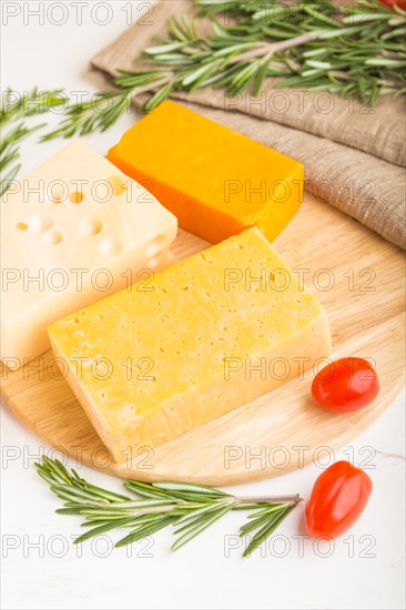 Various types of cheese with rosemary and tomatoes on wooden board on a white wooden background and linen textile. Side view, close up, selective focus