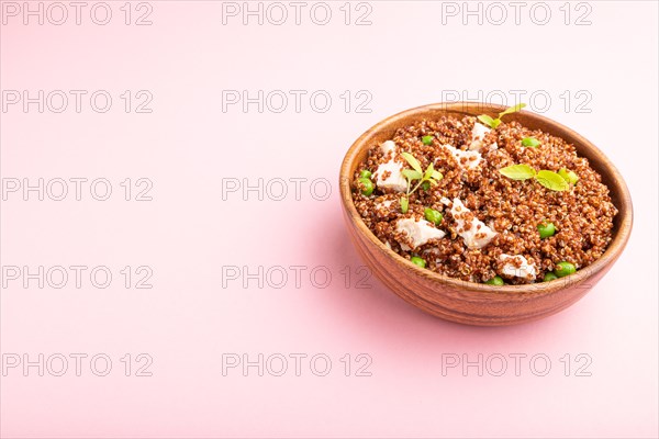 Quinoa porridge with green pea and chicken in wooden bowl on a pastel pink background. Side view, close up, copy space