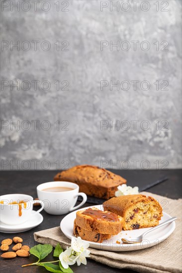 Homemade cake with raisins, almonds, soft caramel and a cup of coffee on a black concrete background and linen textile. Side view, copy space, selective focus