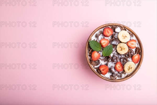 Chocolate cornflakes with milk and strawberry in wooden bowl on pink pastel background. Top view, flat lay, copy space