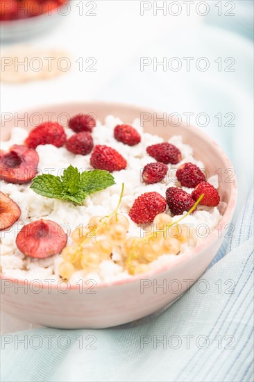 Rice flakes porridge with milk and strawberry in ceramic bowl on white concrete background and blue linen textile. Side view, close up, selective focus