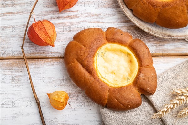 Sour cream bun with cup of coffee on a white wooden background and linen textile. top view, flat lay, close up