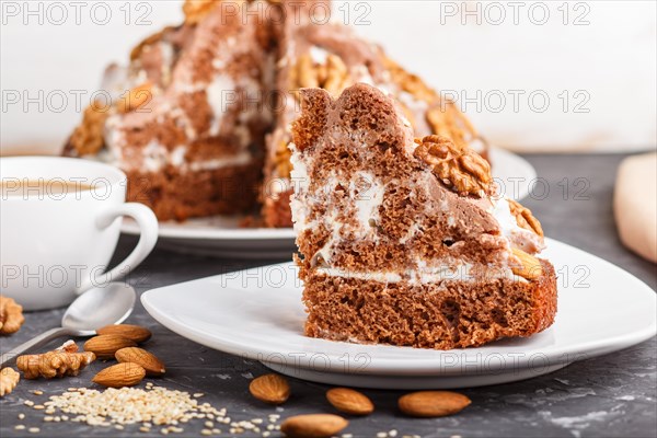 Homemade cake with milk cream, cocoa, almond, hazelnut on a black concrete background and a cup of coffee. Side view, close up, selective focus