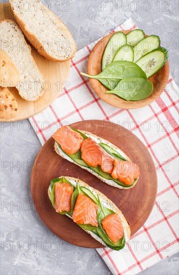 Smoked salmon sandwiches with cucumber and spinach on wooden board on a gray concrete background. top view, flat lay