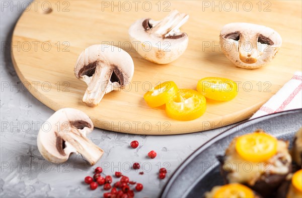 Sliced raw champignons with kumquats on a gray concrete background. ceramic plate, side view, close up, selective focus