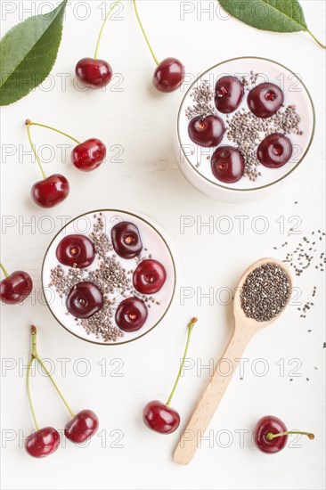 Yoghurt with cherries, chia seeds and granola in glass with wooden spoon on white wooden background. top view, flat lay