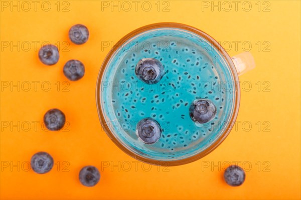 Glass of blueberry blue colored drink with basil seeds on orange background. Morninig, spring, healthy drink concept. Top view, close up, flat lay