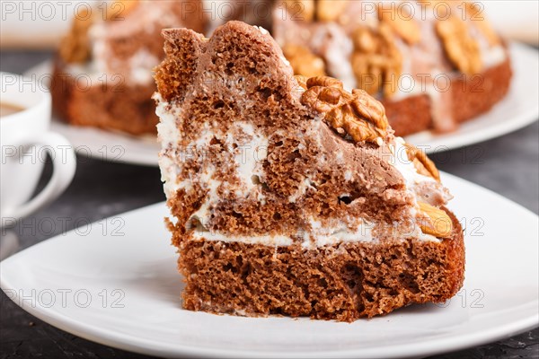Homemade cake with milk cream, cocoa, almond, hazelnut on a black concrete background and a cup of coffee. Side view, close up, selective focus