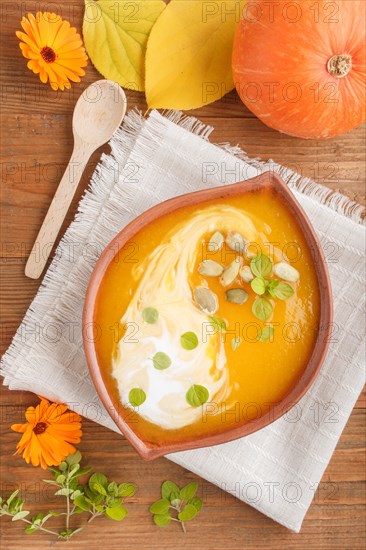 Traditional pumpkin cream soup with seeds in clay bowl on a brown wooden background with linen napkin. top view, flat lay, close up
