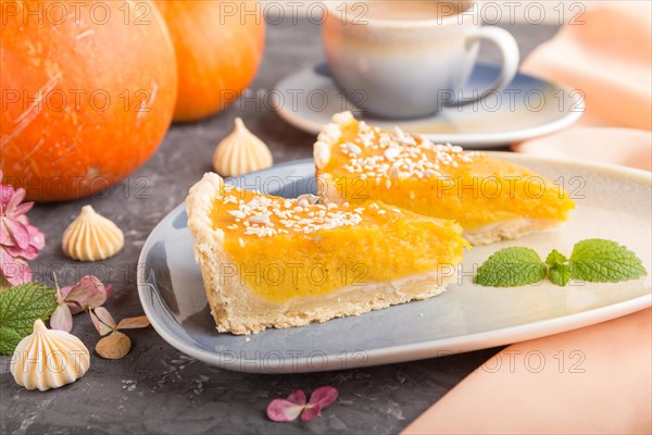 Two pieces of traditional american pumpkin pie with cup of coffee on a black concrete background and orange textile. side view, close up, contrast, selective focus