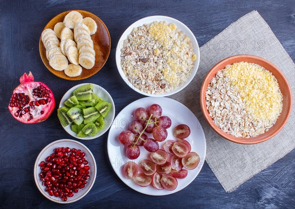 A set of plates with muesli, grapes, kiwi, pomegranate, banana on a black wooden background. top view