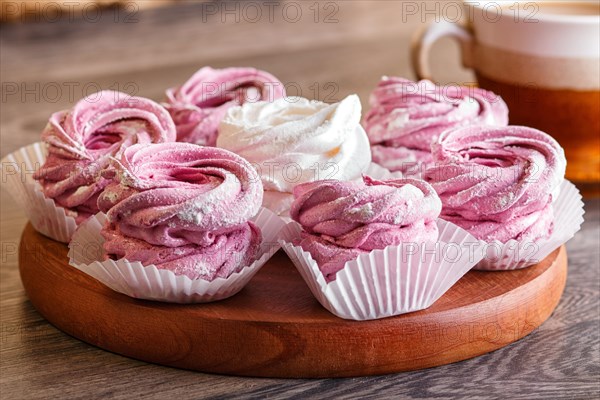 Pink and white marshmallows (zephyr) on a round wooden board with cup of coffee on a gray wooden background