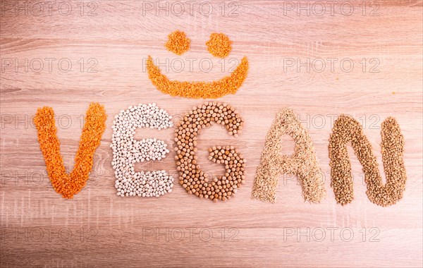 Word Vegan with a smile made of lentils, buckwheat, beans, rice and chickpeas on a wooden background