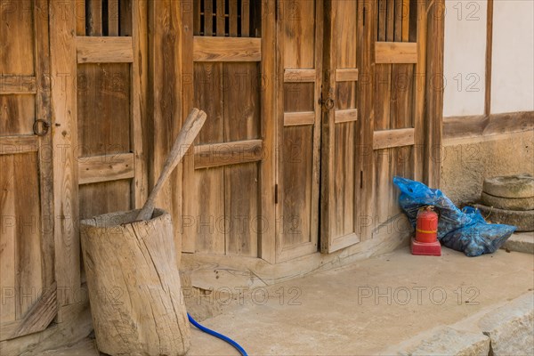 Wooden hand grain pulverizer in front of wooden building in public park displaying traditional Korean architecture in South Korea