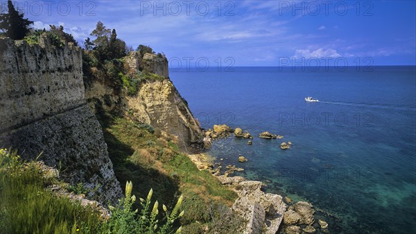 Steep cliffs and old fortress walls overlook the clear blue sea under a partly cloudy sky, sea fortress Methoni, Peloponnese, Greece, Europe