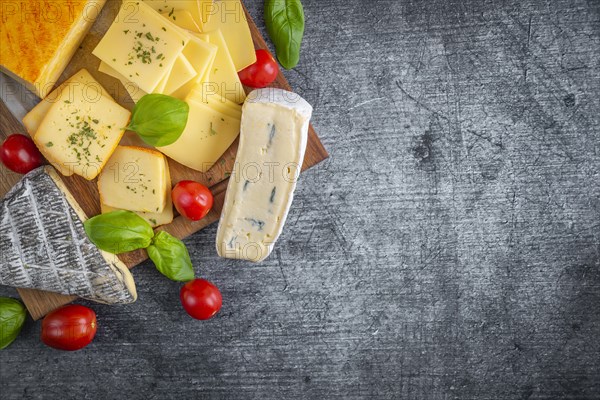 A selection of different cheeses decorated with basil and tomatoes on a wooden board, copy room