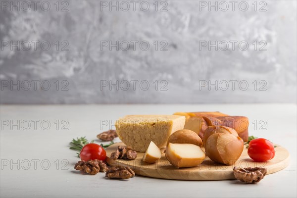 Smoked cheese and various types of cheese with rosemary and tomatoes on wooden board on a gray and white background. Side view, copy space, selective focus