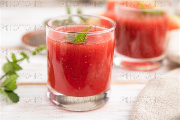 Watermelon juice with chia seeds and mint in glass on a white wooden background with linen textile. Healthy drink concept. Side view, close up, selective focus