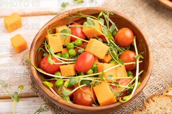 Vegetarian vegetable salad of tomatoes, pumpkin, microgreen pea sprouts on white wooden background and linen textile. Side view, close up, selective focus