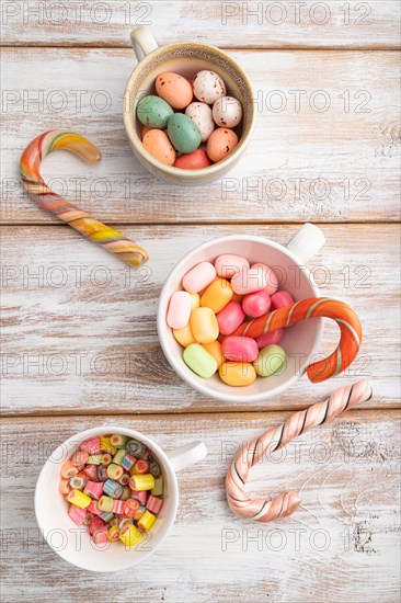 Heap of multicolored caramel candies in cups on white wooden background. close up, top view, flat lay