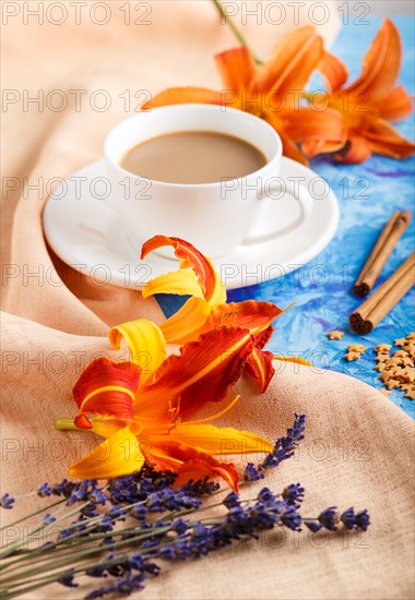 Orange day-lily and lavender flowers and a cup of coffee on a blue concrete background, with orange textile. Morninig, spring, fashion composition. side view, selective focus