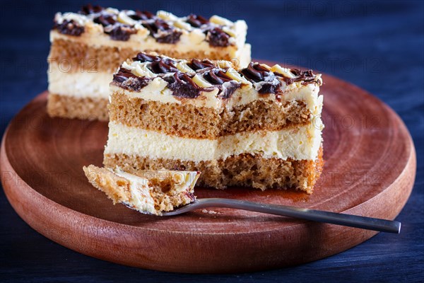 A piece of cake with milk and butter cream cutted with spoon on a wooden kitchen board, close up, selective focus, black background