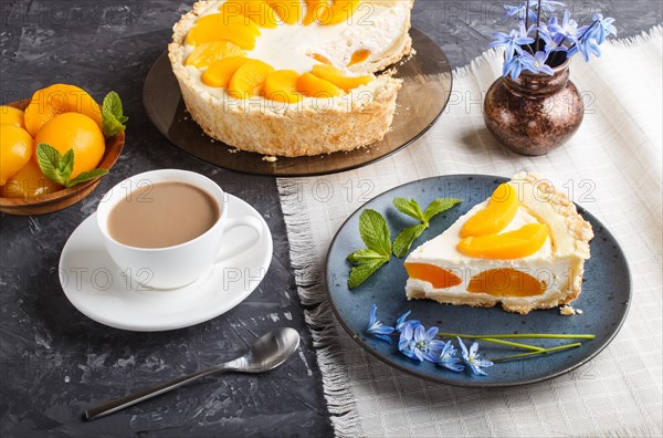 A piece of peach cheesecake on a blue ceramic plate with blue flowers and a cup of coffee on a linen napkin on a black concrete background. side view, close up