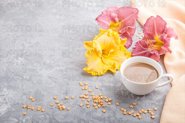 Yellow anf purple day-lilies cup of coffee on a gray concrete background, with orange textile. Morninig, spring, fashion composition, side view, copy space