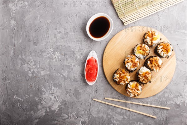 Japanese maki sushi rolls with cream cheese, chopsticks, soy sauce and marinated ginger on wooden board on a gray concrete background. Top view, flat lay, copy space