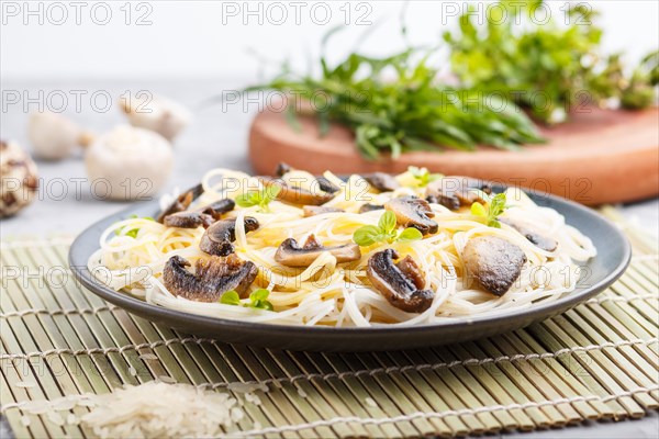 Rice noodles with champignons mushrooms, egg sauce and oregano on blue ceramic plate on a gray concrete background. side view, close up, selective focus