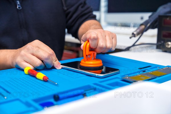 Unrecognizable male technician opening the screen of a mobile using suction cup in a small workshop