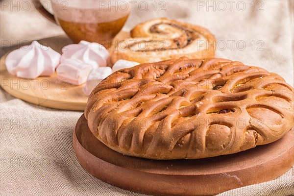 Sweet buns, meringues and coffee cup on a wooden board and linen tablecloth