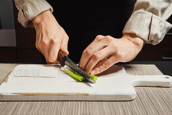 Unrecognizable woman slicing spring onion into thin strips