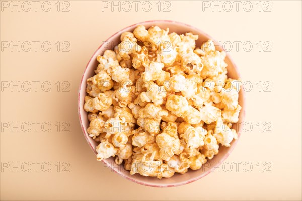 Popcorn with caramel in ceramic bowl on pastel orange background. Top view, flat lay, close up