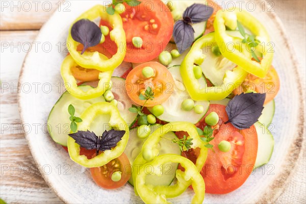 Vegetarian salad from green pea, tomatoes, pepper and basil on white wooden background and linen textile. top view, close up, flat lay, selective focus