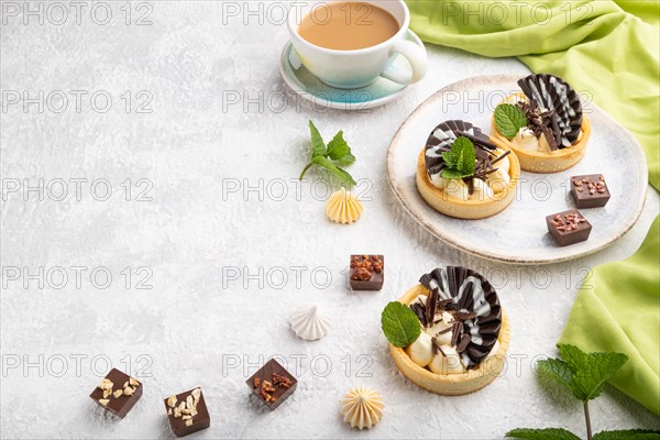 Sweet tartlets with chocolate and cheese cream with cup of coffee on a gray concrete background and green textile. Side view, flat lay, copy space