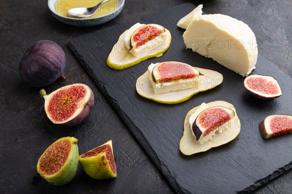 Summer appetizer with pear, cottage cheese, figs and honey on slate board on a black concrete background. Side view, close up