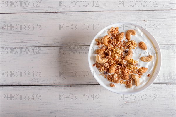 White plate with greek yogurt, granola, almond, cashew, walnuts on white wooden background. top view. copy space