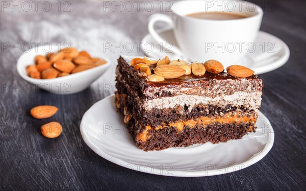 Chocolate cake with caramel, peanuts and almonds on a black wooden background. cup of coffee, close up